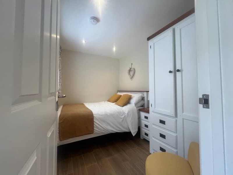 Double bedroom with white wardrobe and mustard cushions